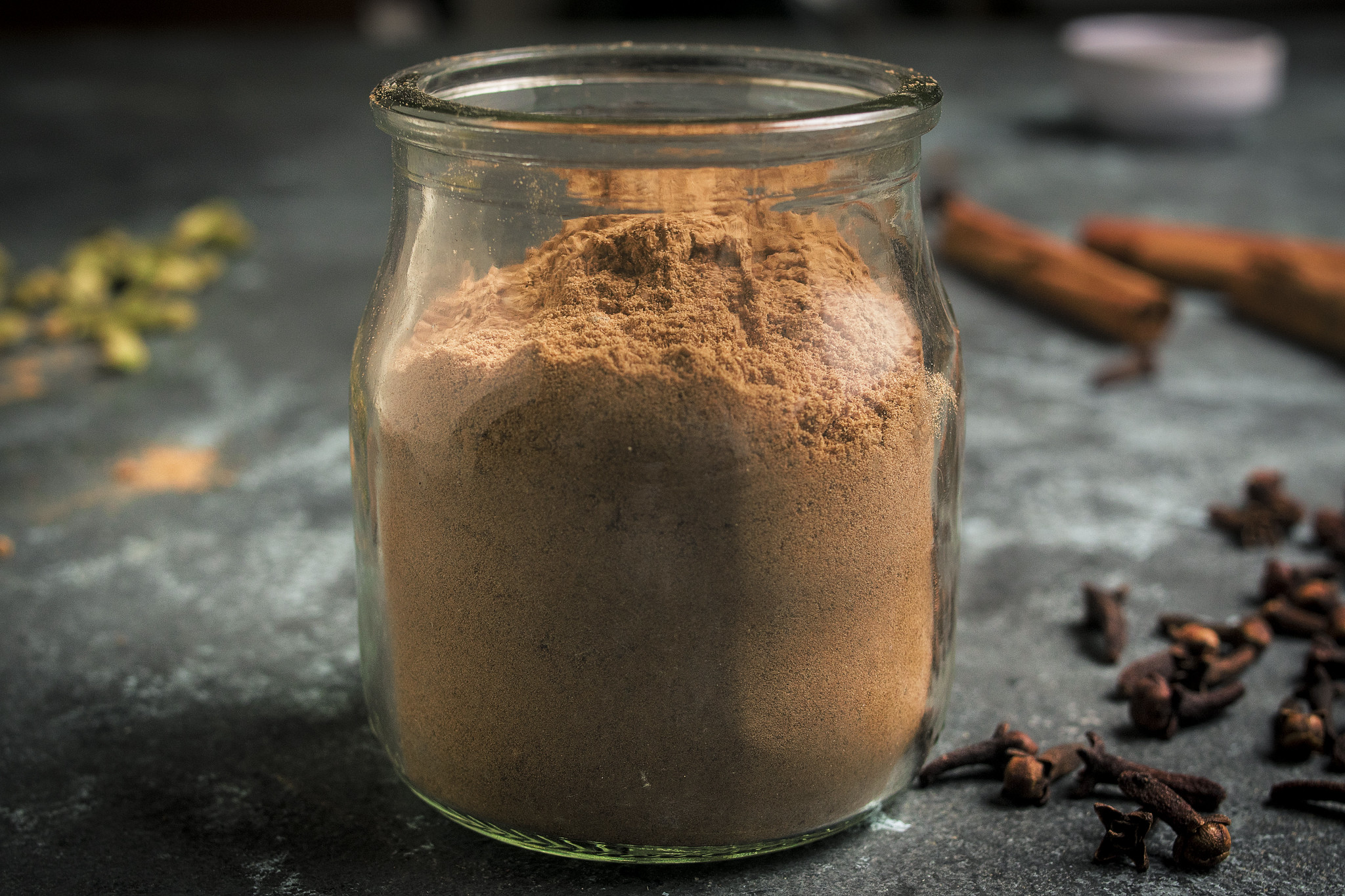Homemade pumpkin pie spice stored in a glass jar with cloves and cinnamon sticks nearby.